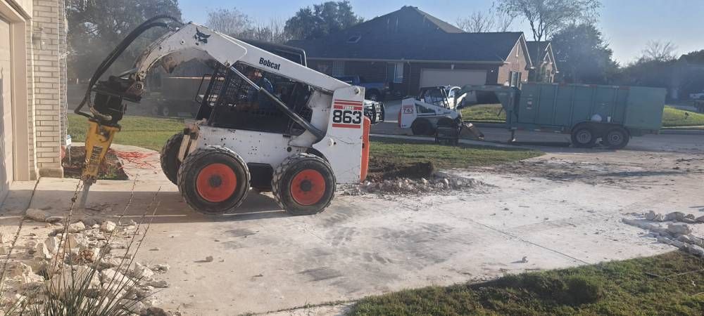 A bobcat is driving down a driveway next to a house.