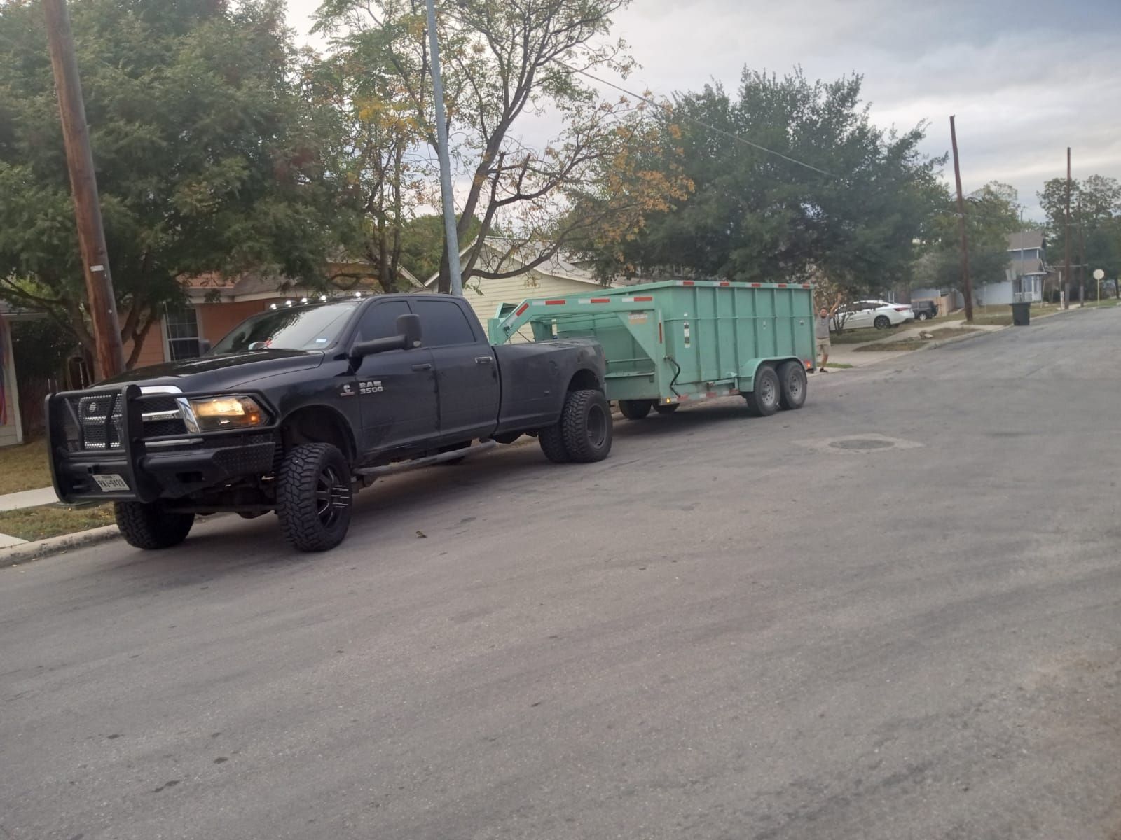 A black truck is pulling a green trailer down a street