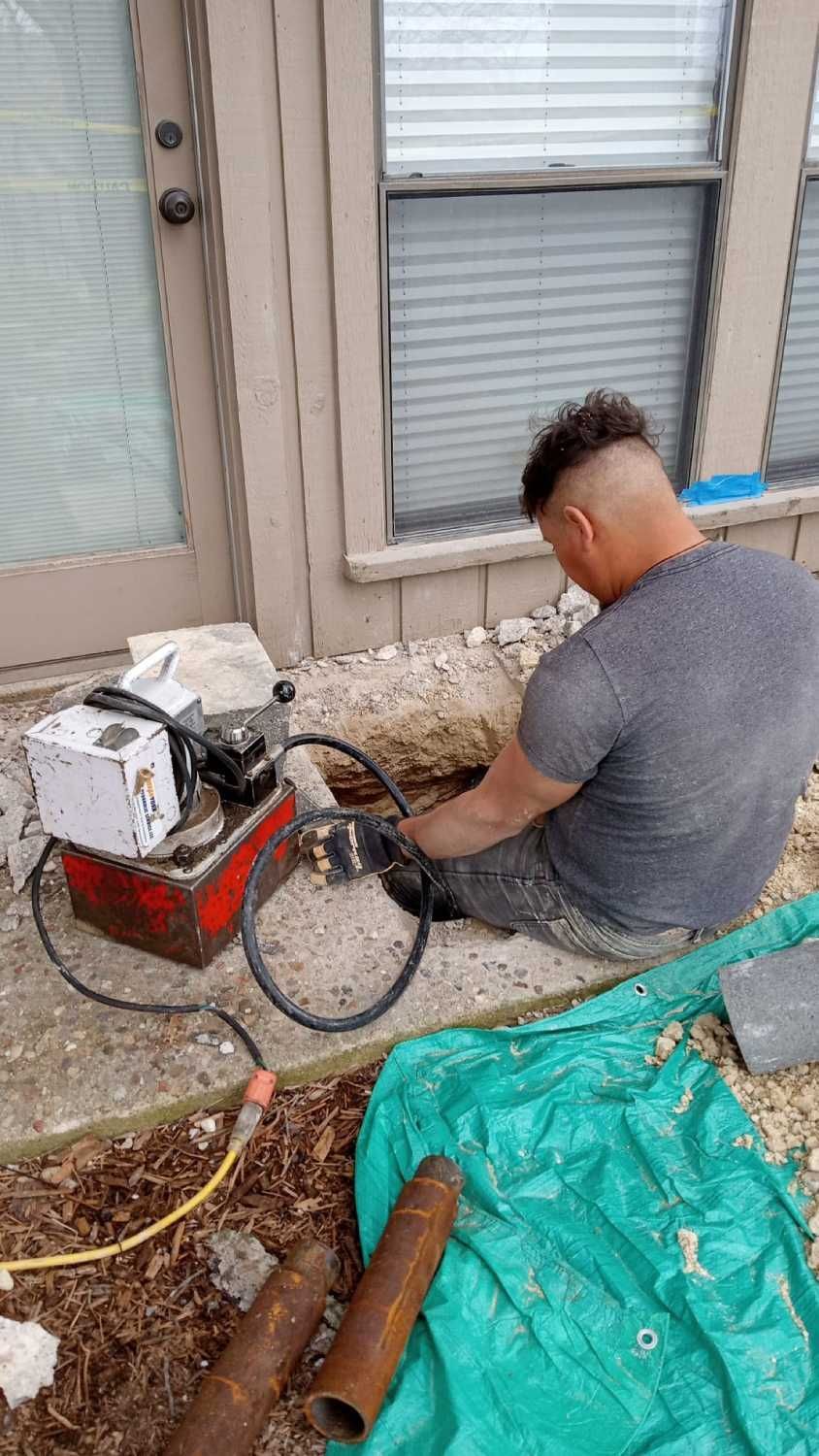 A man is sitting on the ground working on a pipe.