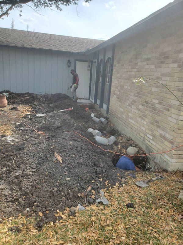 A man is digging in the dirt in front of a brick house.