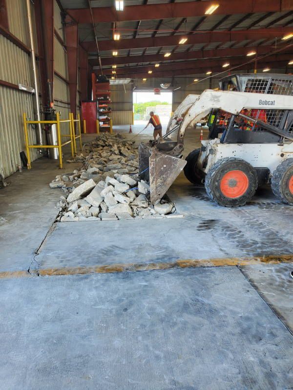 A bobcat is being used to remove concrete in a warehouse.