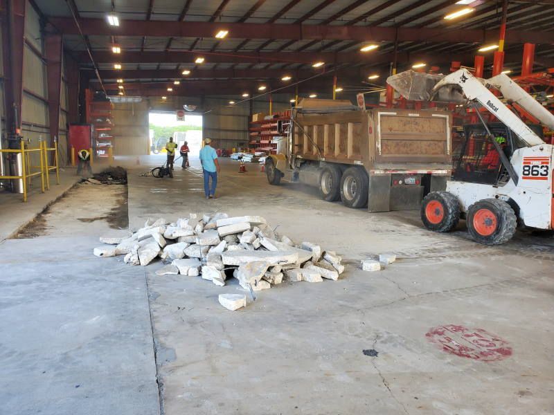 A bobcat is parked in a warehouse next to a dump truck