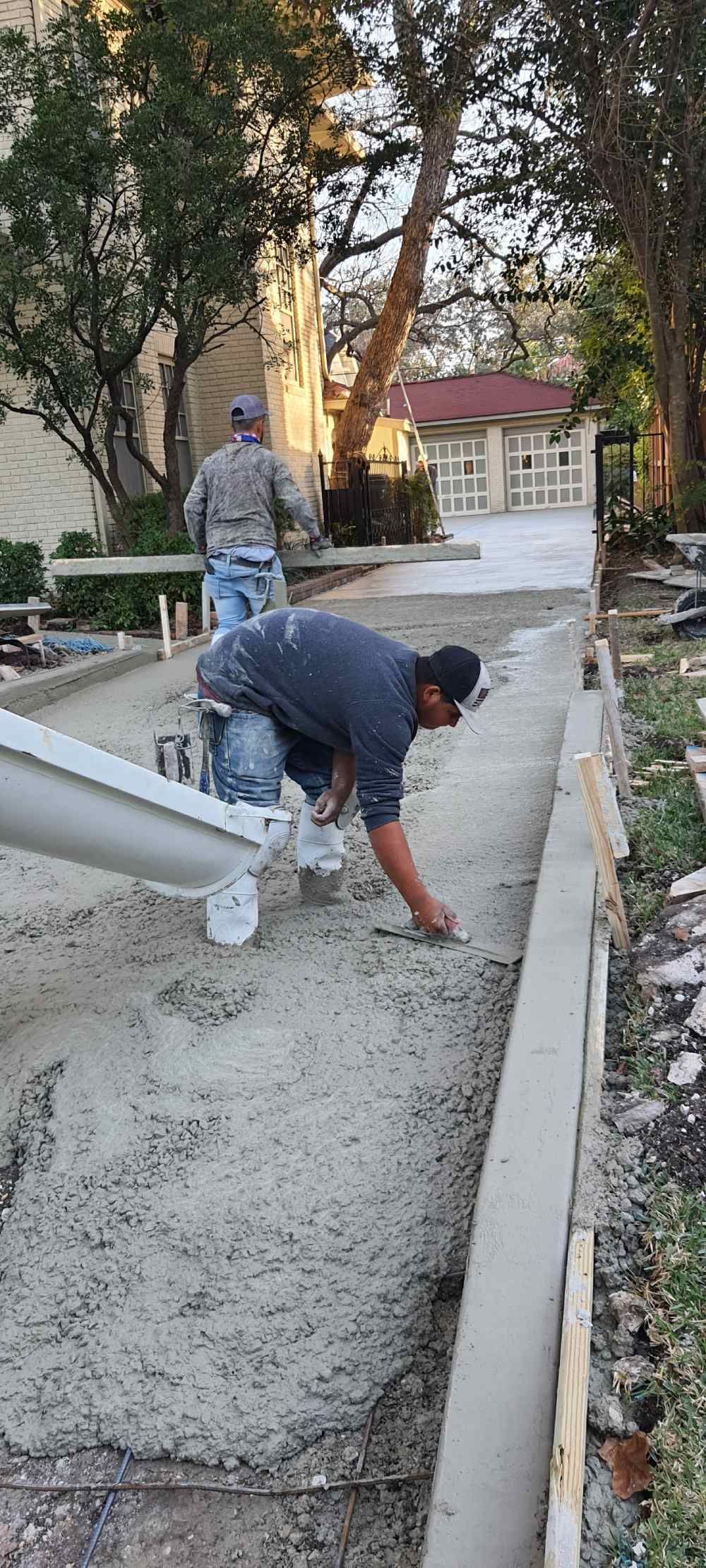 A man is laying concrete on the side of a road.