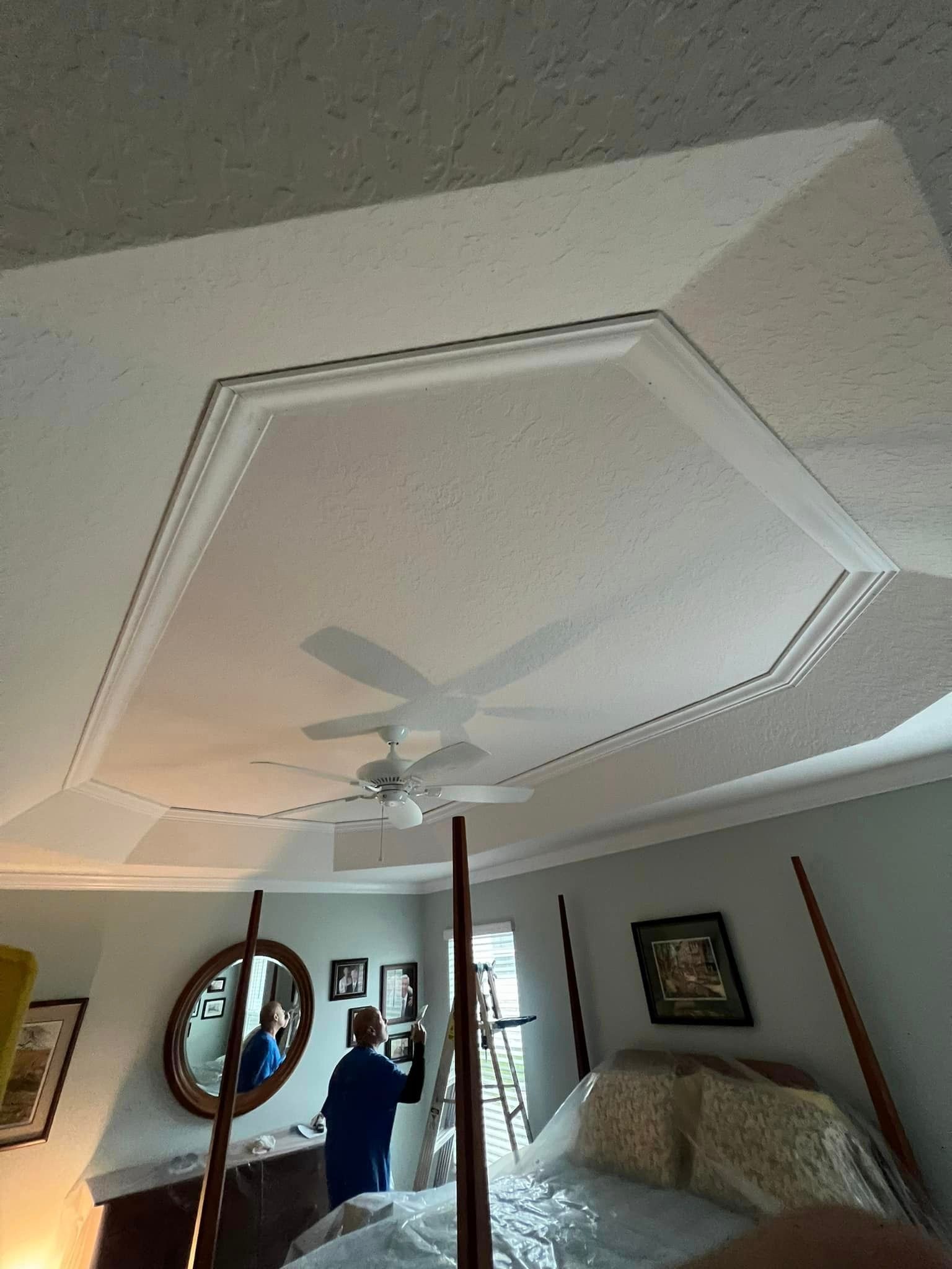 A man is standing in a bedroom with a four poster bed and a ceiling fan.