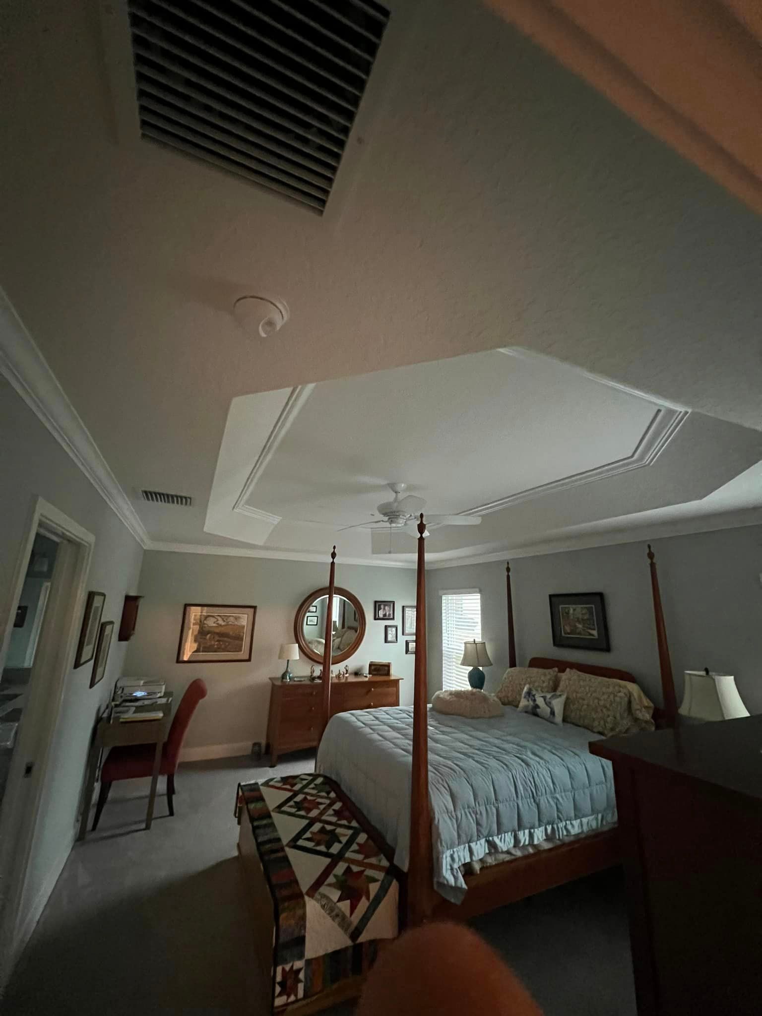 A bedroom with a four poster bed , dresser , desk and ceiling fan.