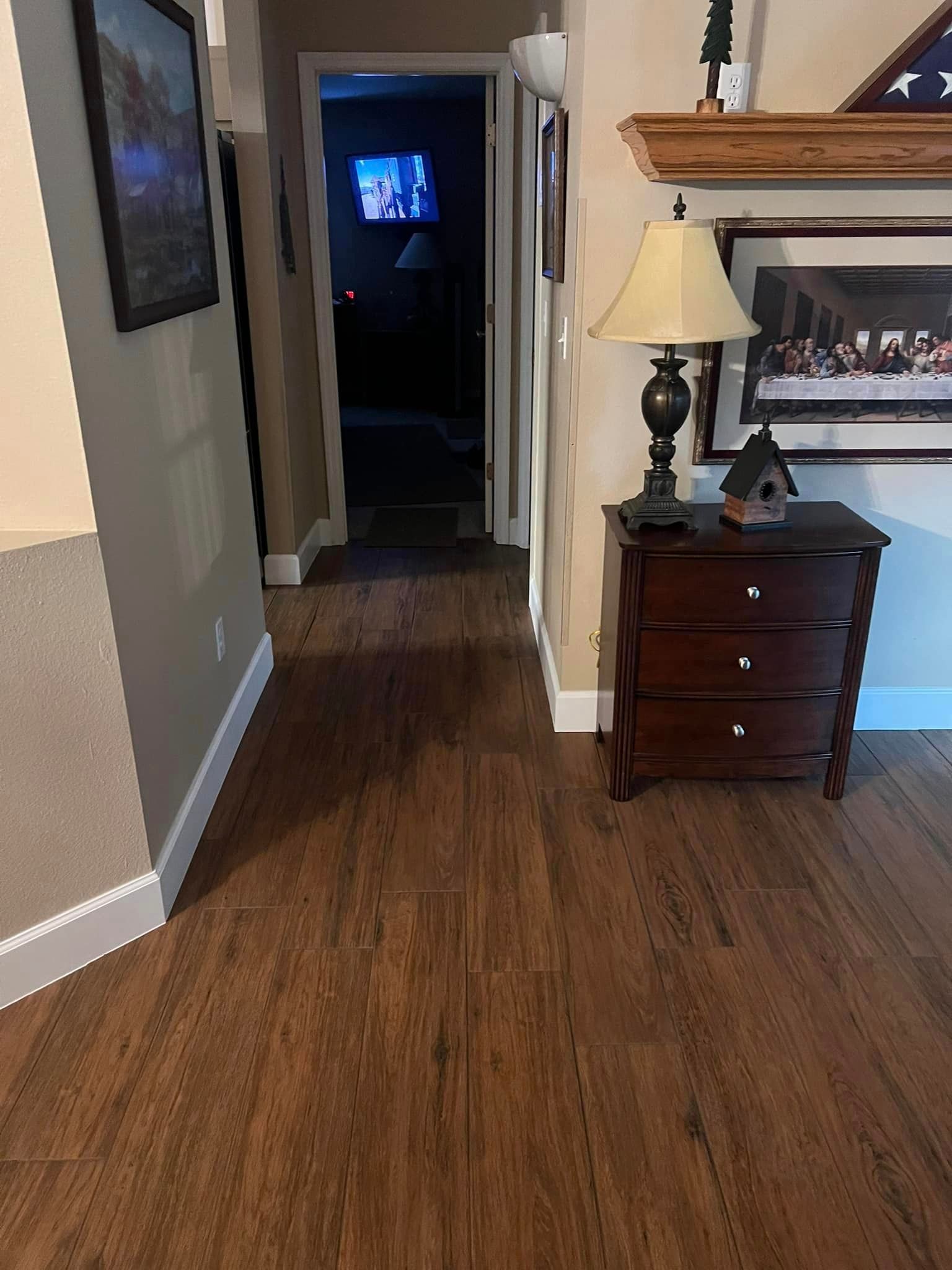 A living room with hardwood floors , a lamp , and a dresser.