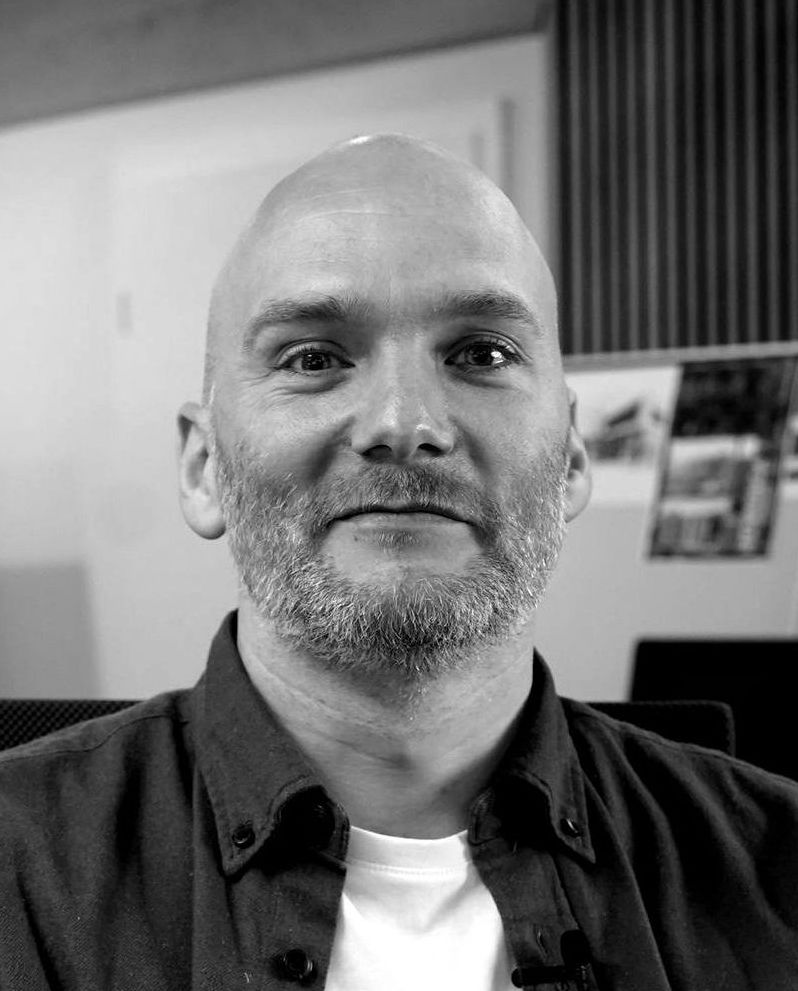 Auf einem Schwarzweißfoto blickt ein glatzköpfiger Mann mit Bart in die Kamera.