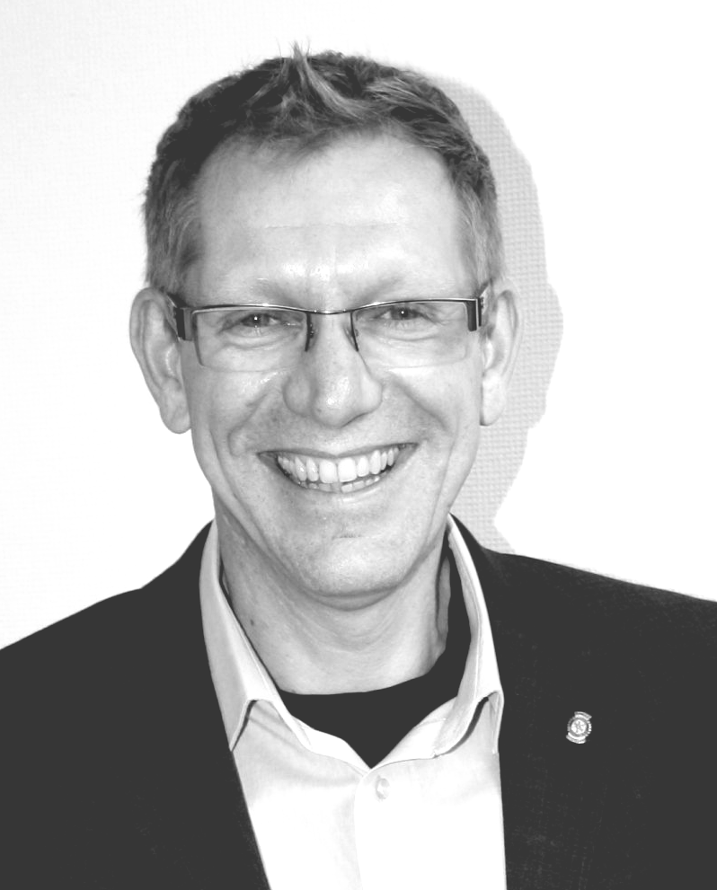 Ein Mann mit Brille und Anzug lächelt auf einem Schwarzweißfoto