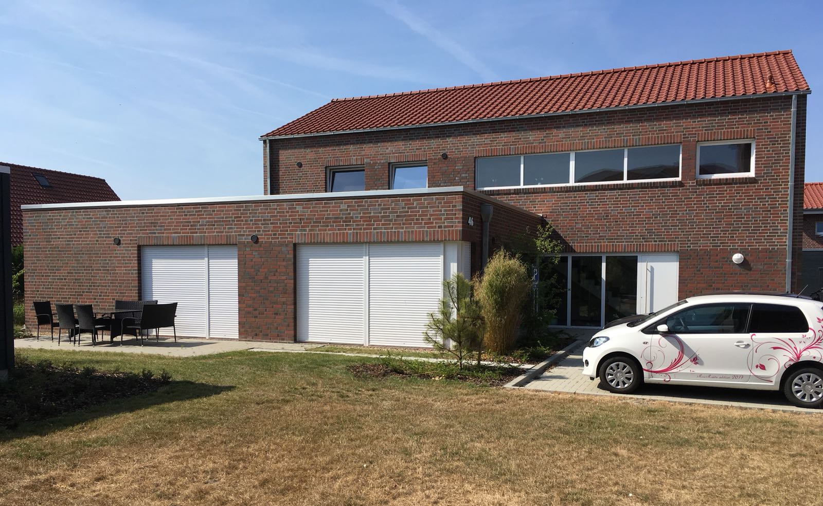 Vor einem großen Backsteinhaus parkt ein weißes Auto.