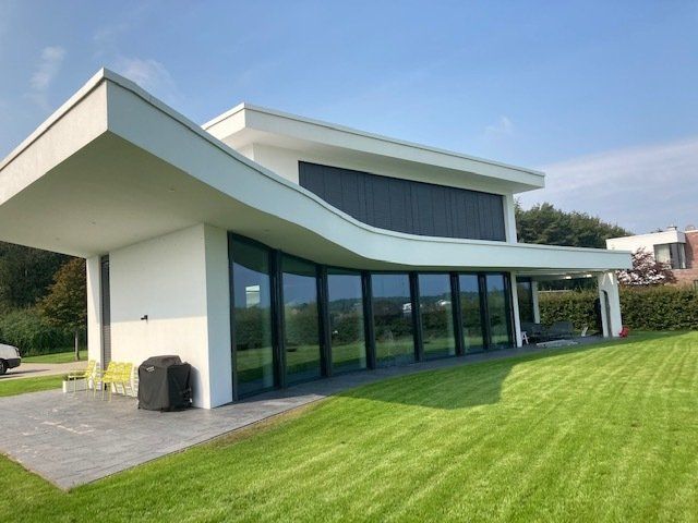 Auf einem üppigen grünen Rasen steht ein weißes Haus mit geschwungenem Dach und vielen Fenstern.