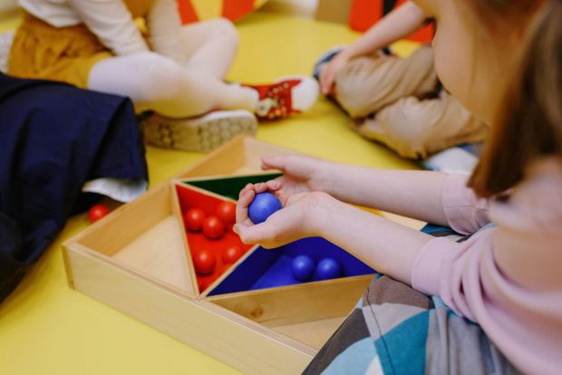Niños clasificando pelotas de colores en recipientes en una mesa durante una actividad en el aula.