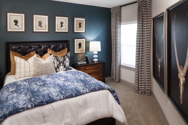 A bedroom with a bed , nightstand , lamp and paintings on the wall.