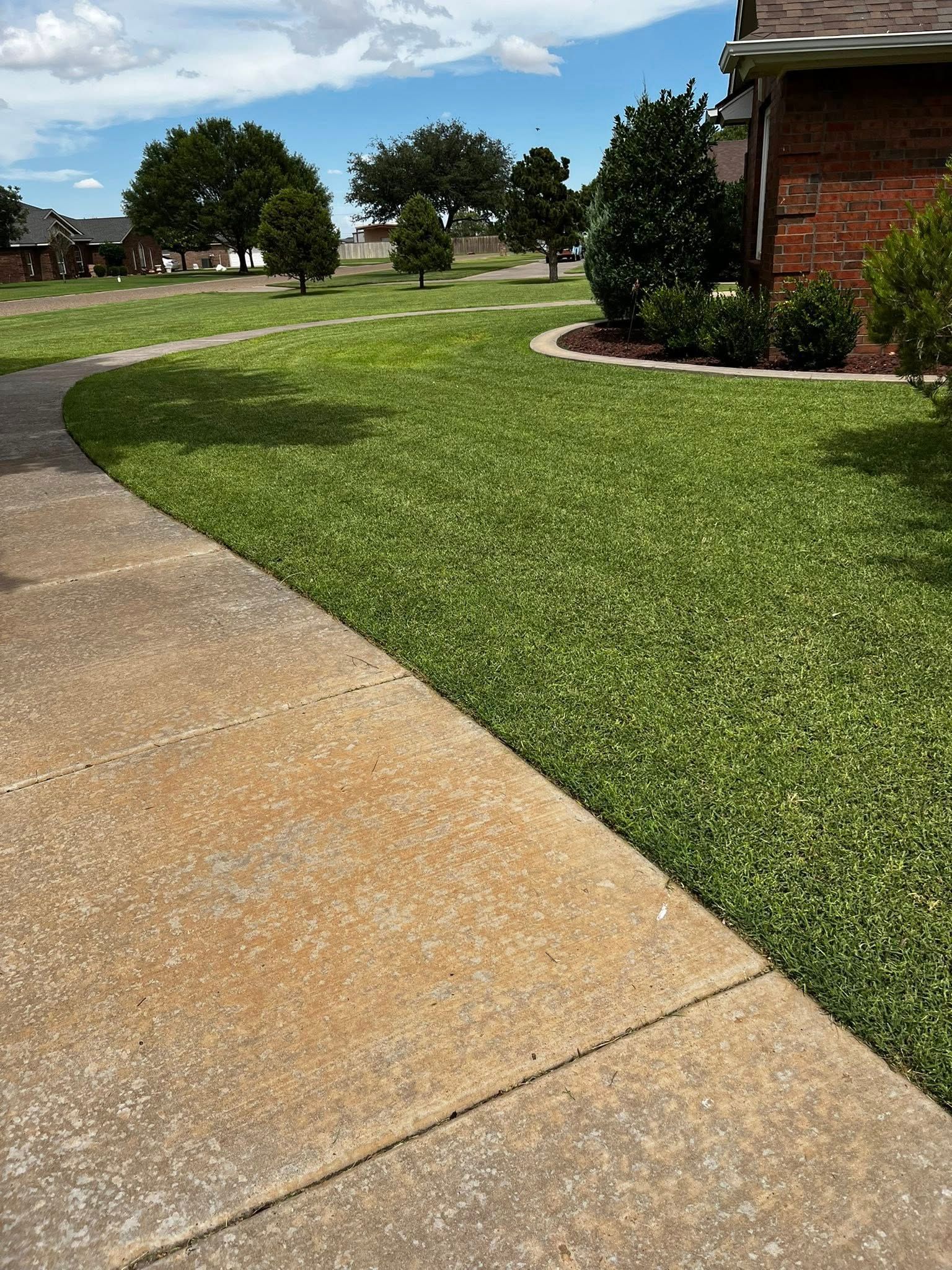 A sidewalk leading to a lush green lawn next to a house.