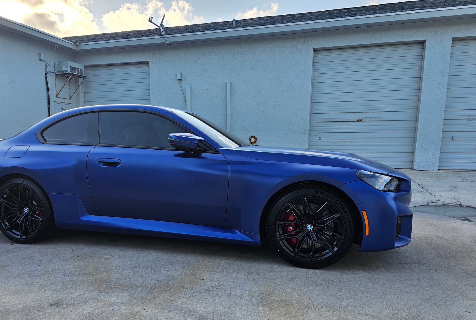 Blue BMW coupe parked in front of a building with garage doors.