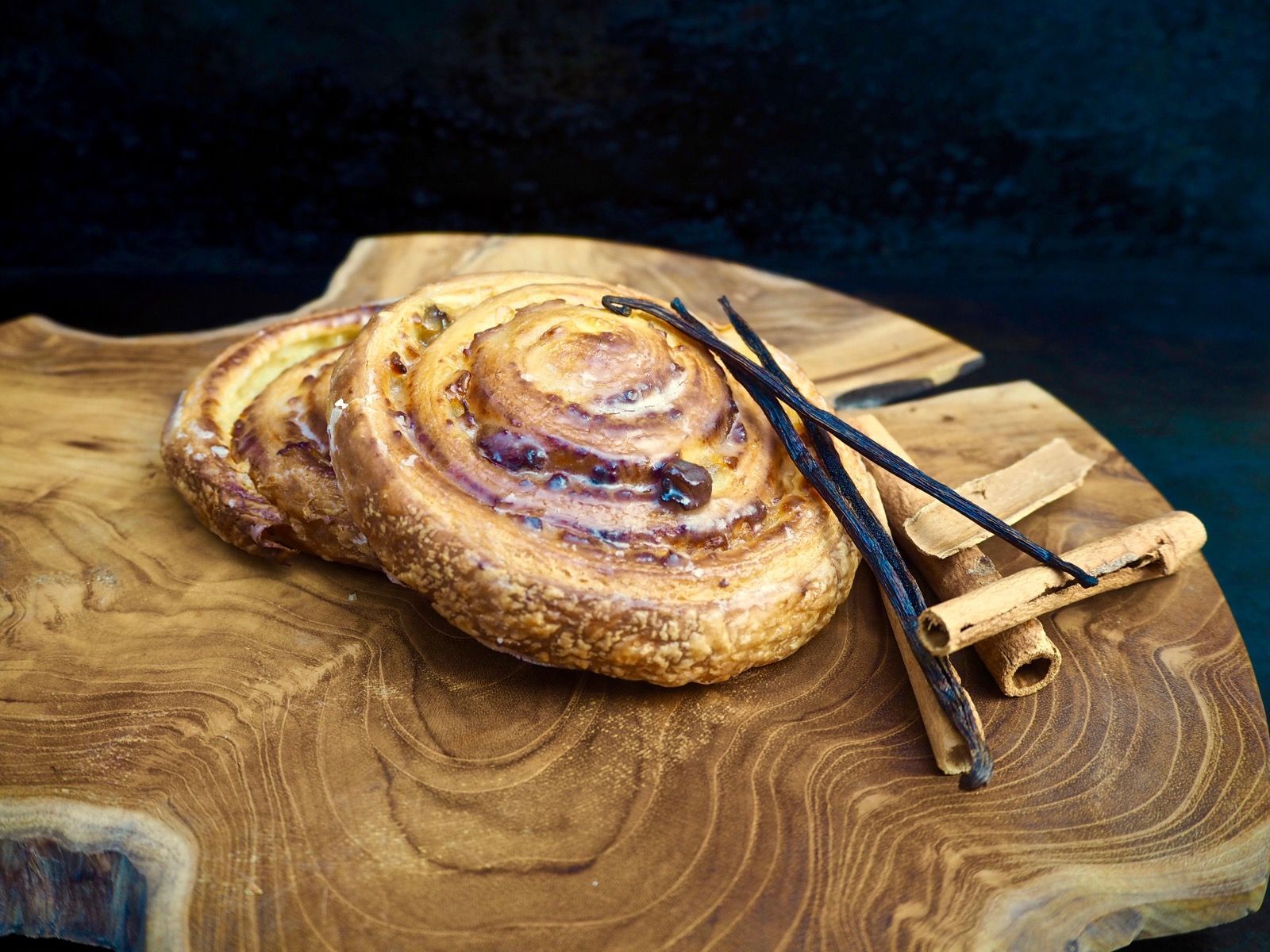 Cinnamon roll with vanilla beans and cinnamon sticks on a wooden board.