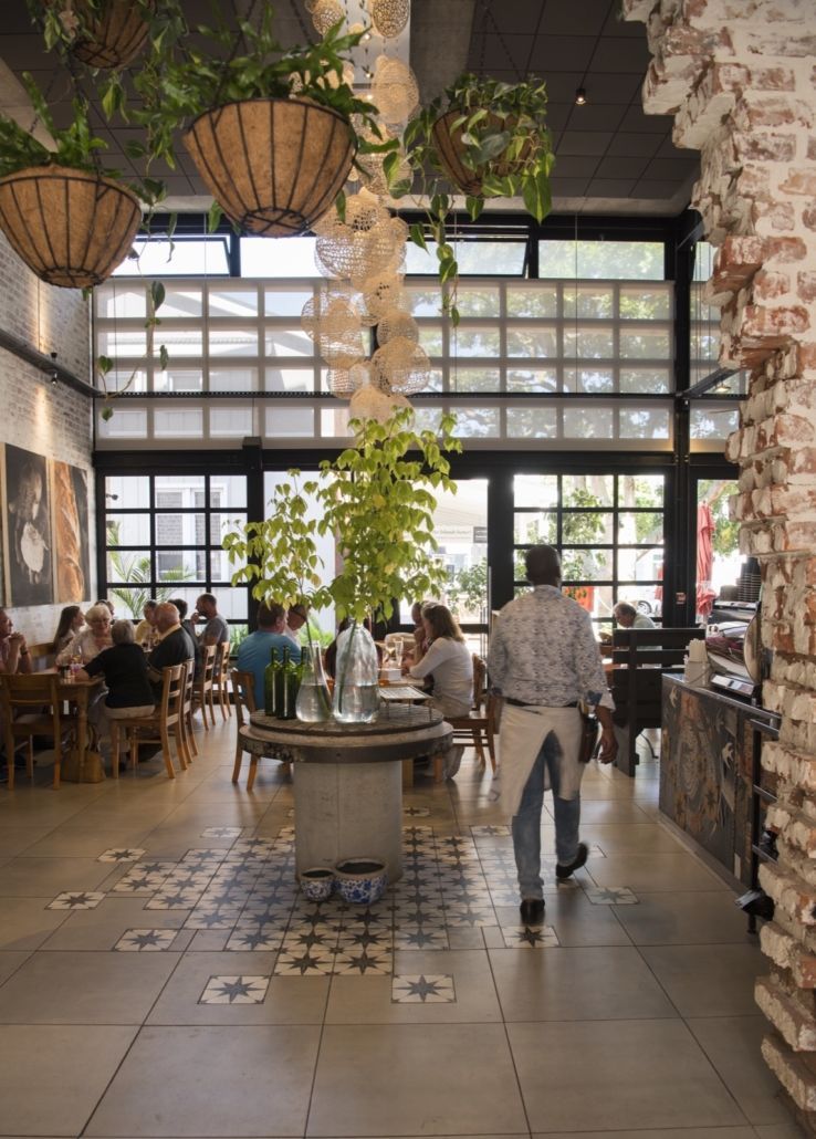Restaurant interior with hanging plants, brick pillar, and a person walking towards the back.