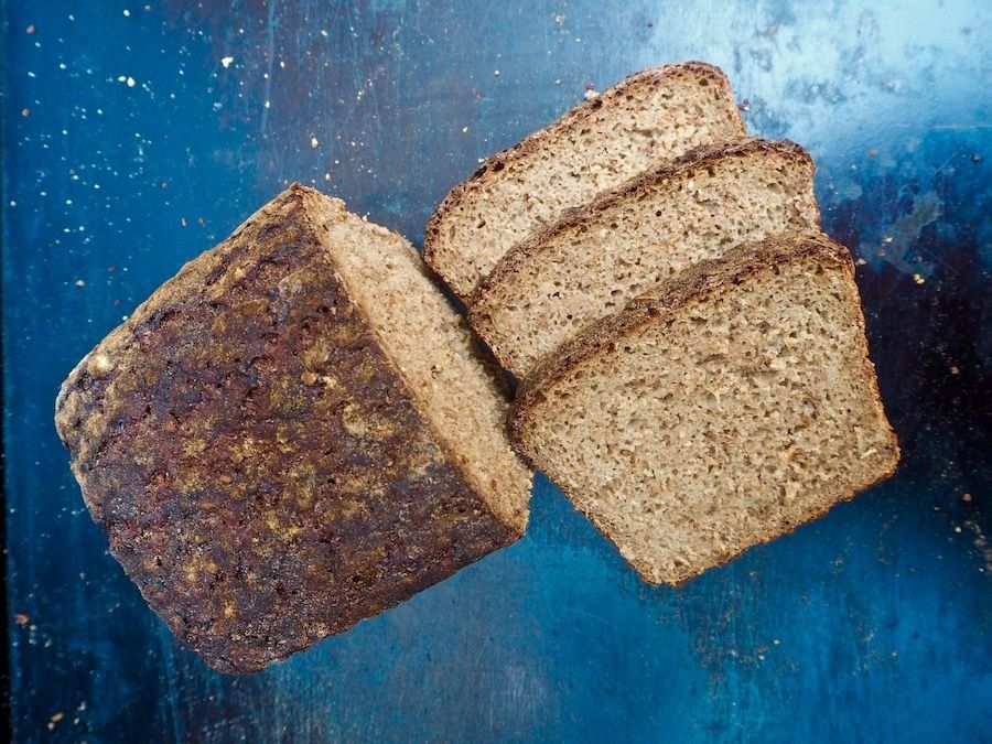 Loaf of sliced dark rye bread on a blue, textured surface.