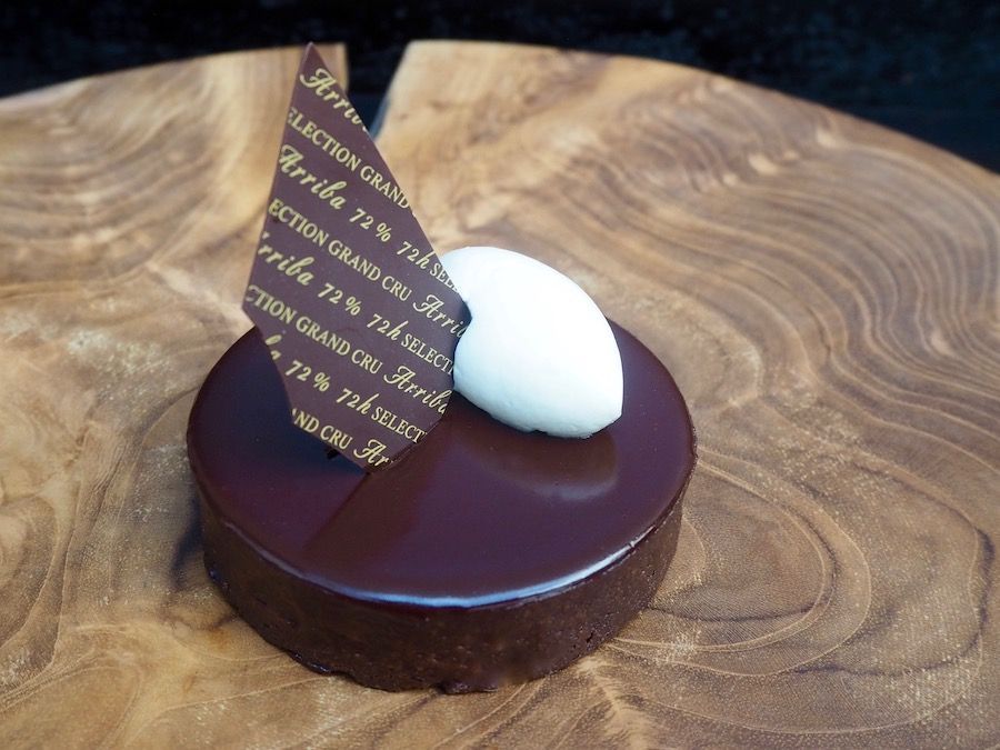 Chocolate dessert on wood, topped with white cream and chocolate garnish.