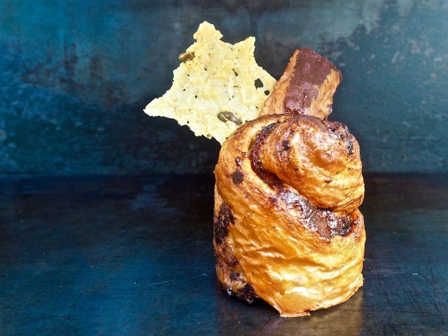 Close-up of a golden-brown pastry with chocolate chips, a crunchy cookie, against a dark blue background.