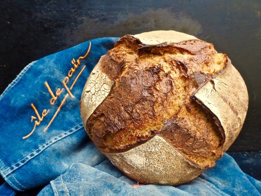 Crusty, round loaf of bread with crisscross cut, on a blue cloth with