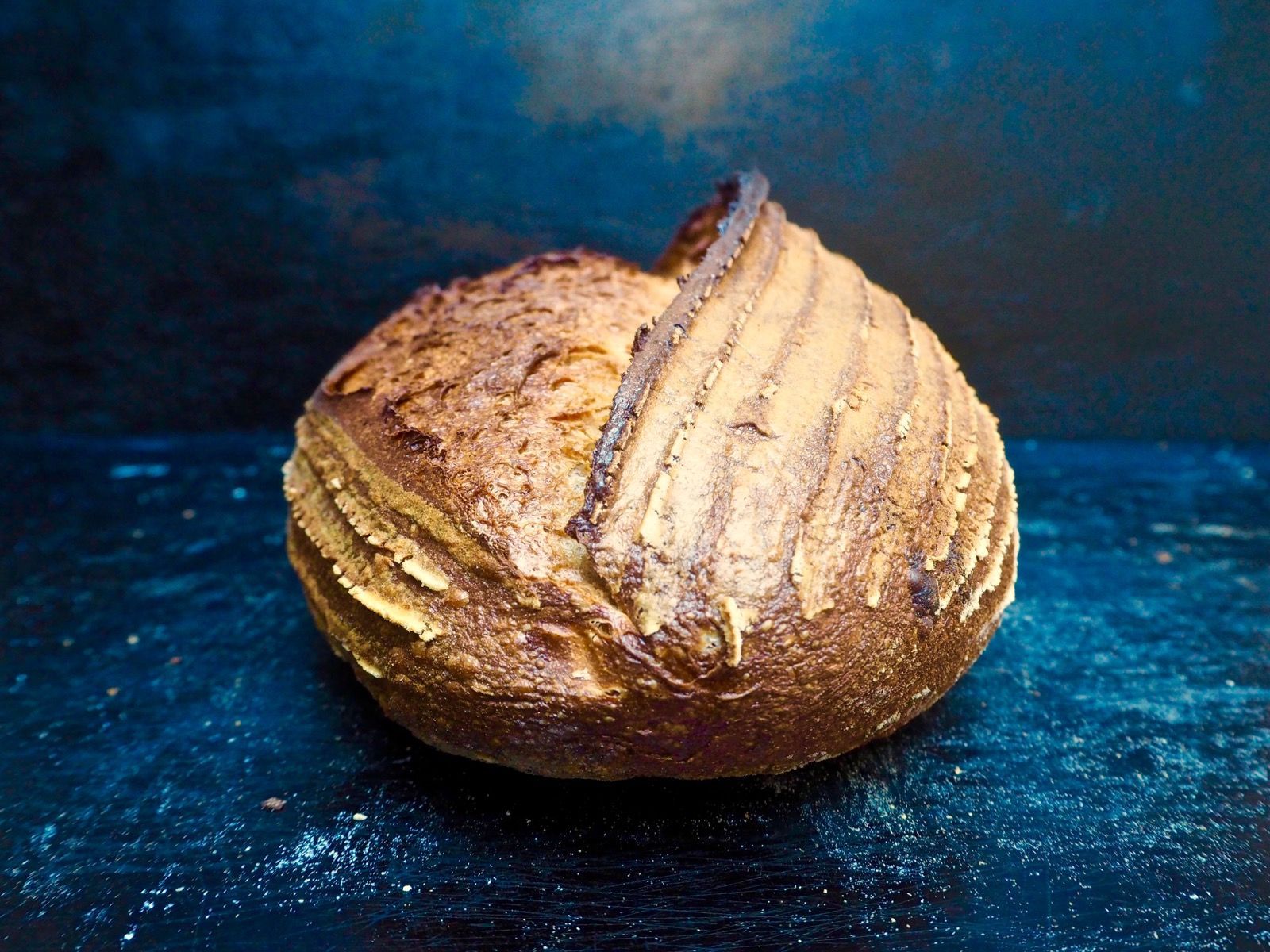 Round loaf of crusty bread with a dark brown exterior on a blue surface.