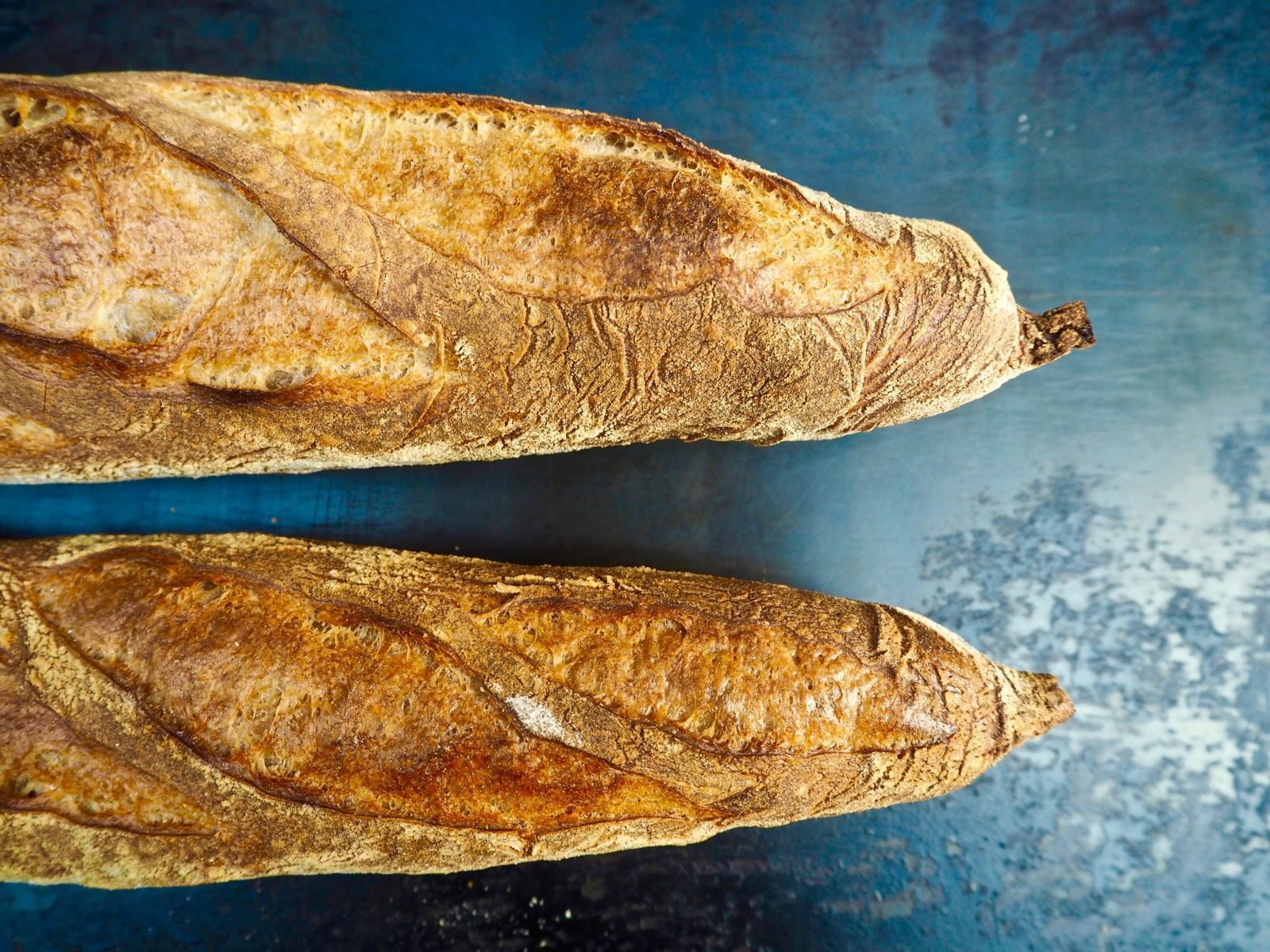 Two crusty baguettes on a dark blue surface, golden brown and textured.