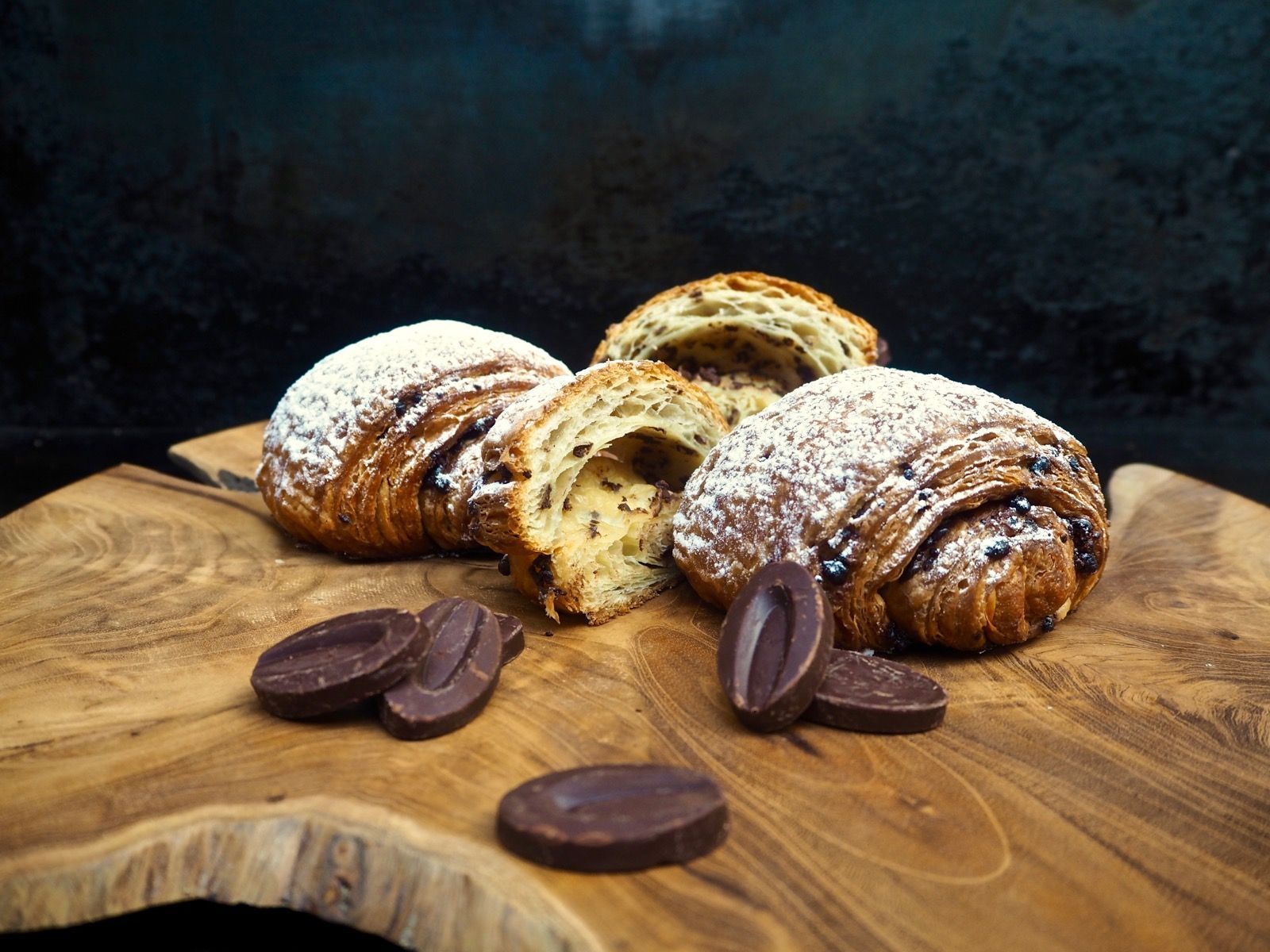 Chocolate croissants on a wooden board with dark chocolate pieces.