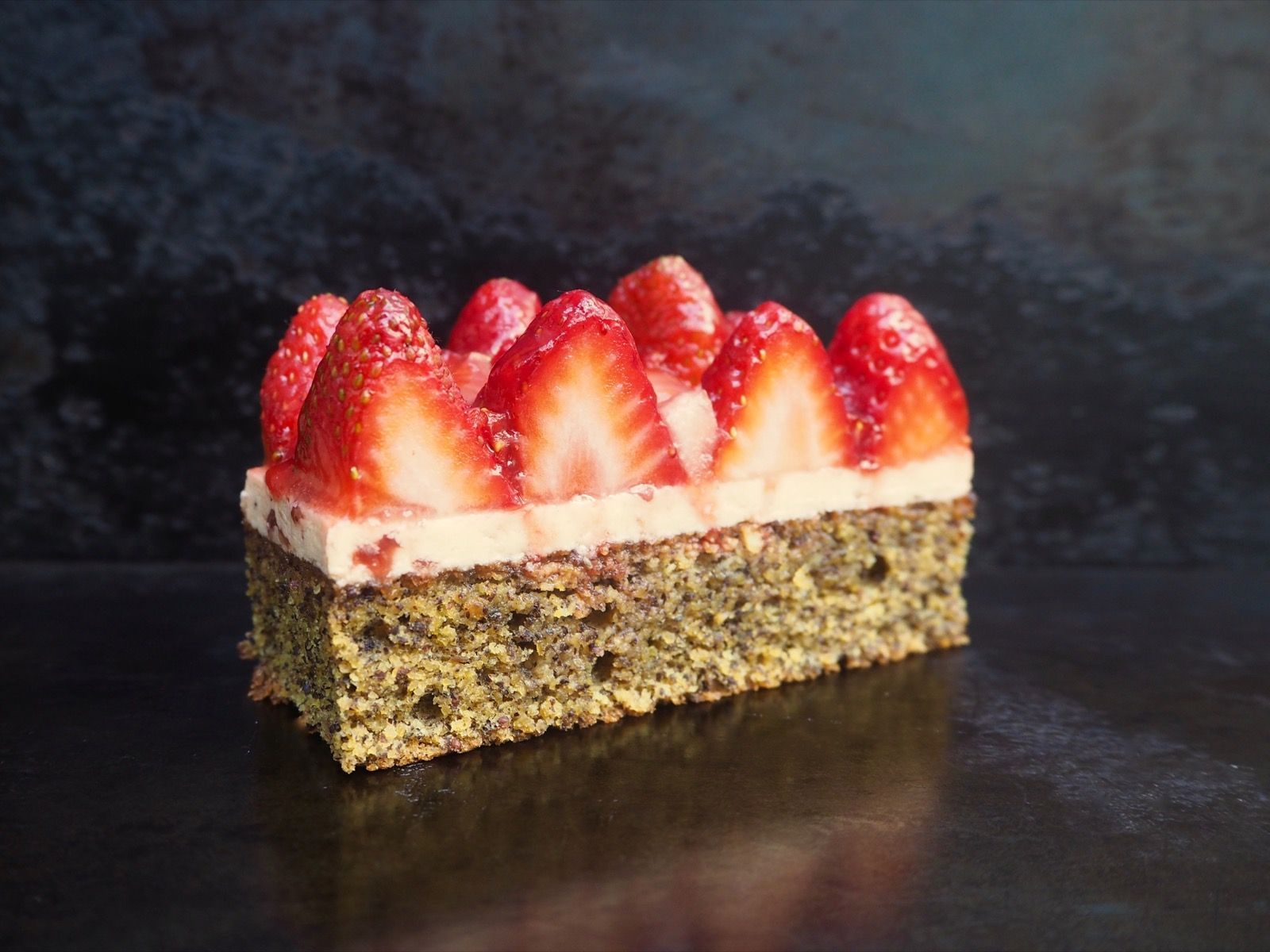 Strawberry tart with fresh berries, atop a cream layer, on a dark background.