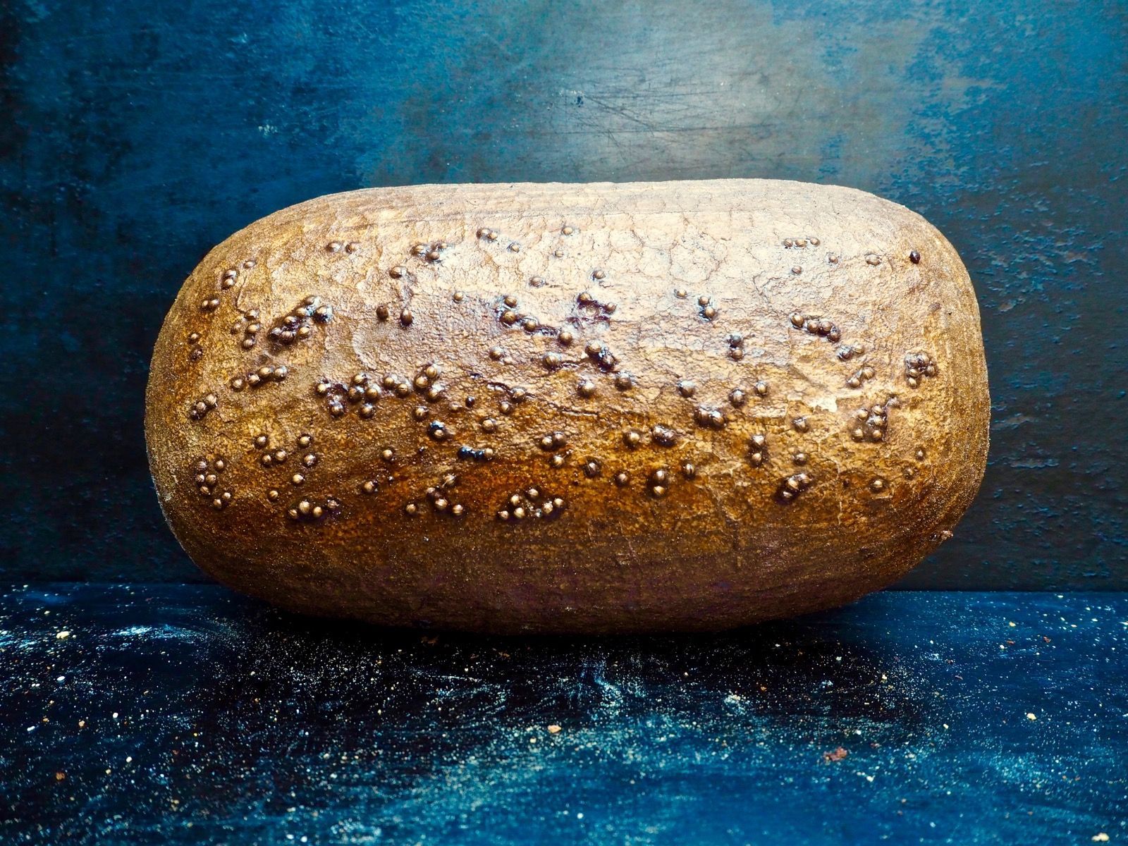 A loaf of rustic brown bread with bumpy texture on a dark blue background.