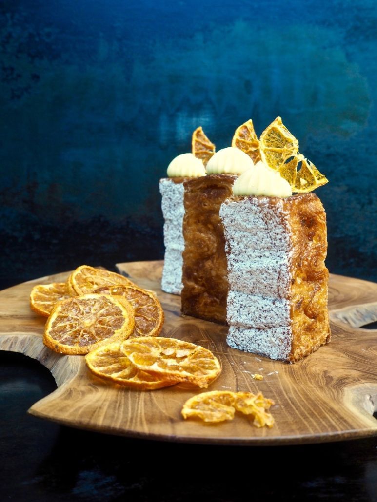 Lemon cake slices with dried citrus and frosting on a wooden board, against a blue backdrop.