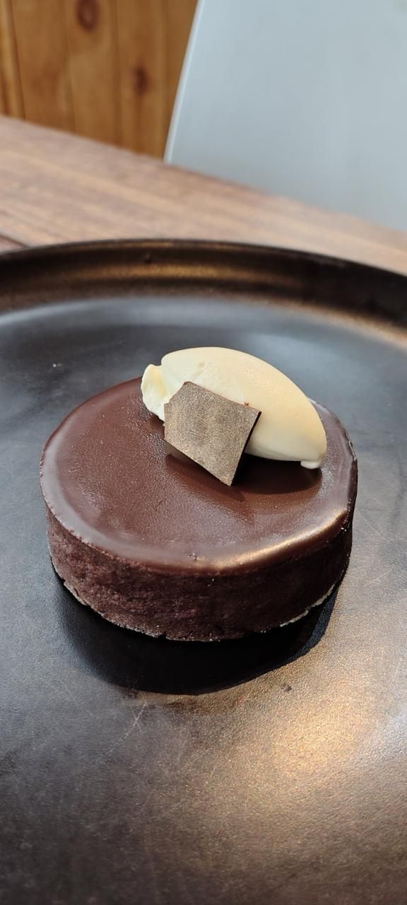 Chocolate tart with white cream and a chocolate piece on a white plate, on a wooden table.