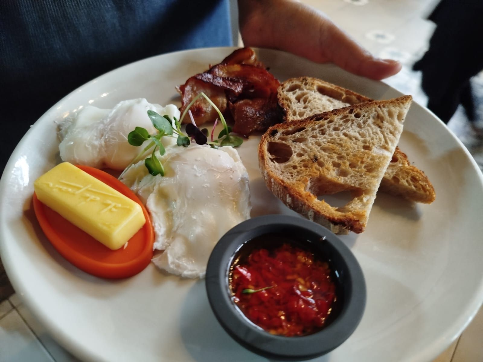Person holding a copper pan with cooked fish rolls, lemon slices, and a topping; wearing an apron.