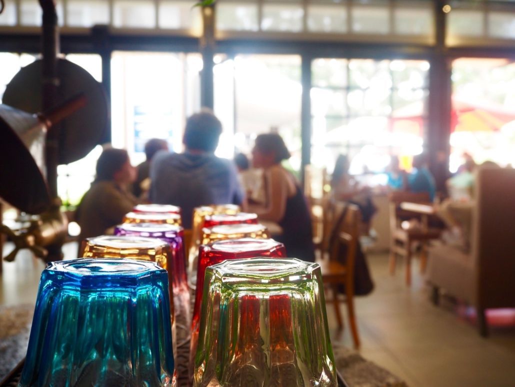 Colorful glasses in a row at a restaurant with people blurred in the background.