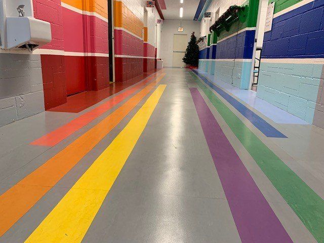 A long school hallway with a rainbow-striped floor and color-blocked walls: red, pink, blue, and green.