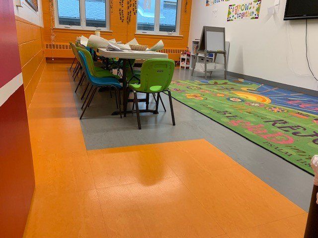Classroom with orange floor, table with chairs, and a colorful rug.