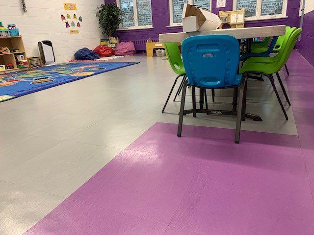 A preschool classroom with colorful furniture, toys, a rug, and a purple and gray floor.