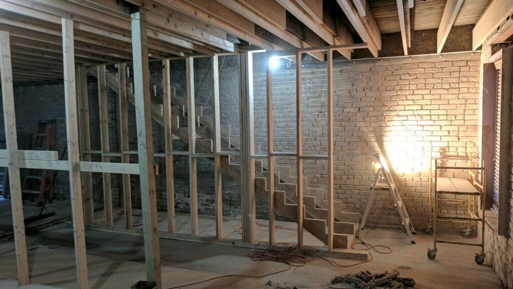 Basement under construction; exposed wooden framing, stairs, brick walls.