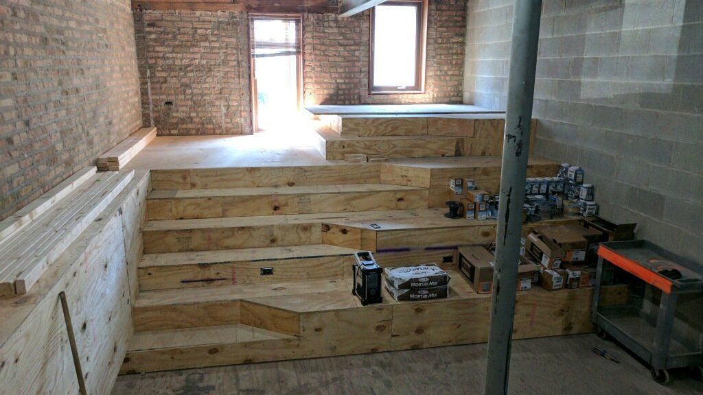 Interior with wooden stairs and stage, exposed brick walls, construction in progress.