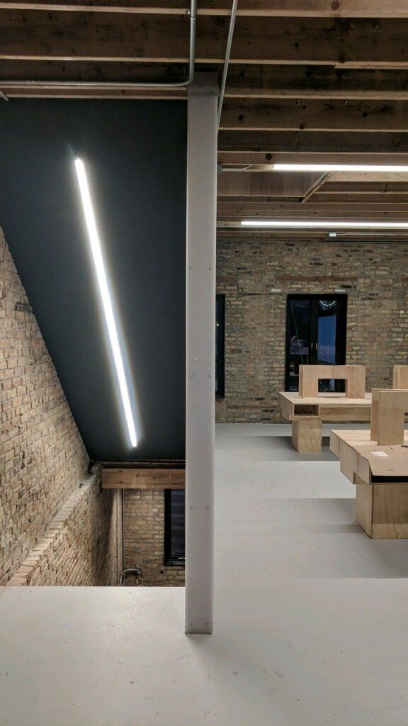 Interior view of a modern office with exposed brick, a white support column, and long fluorescent lights.