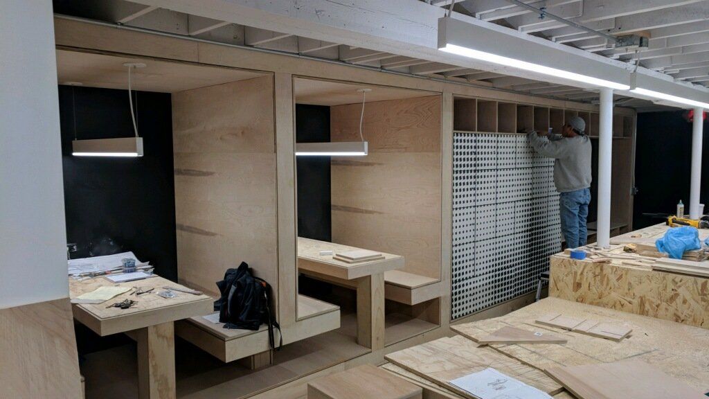 Construction of plywood booths with built-in tables; a worker installs wall panels in a brightly lit interior.