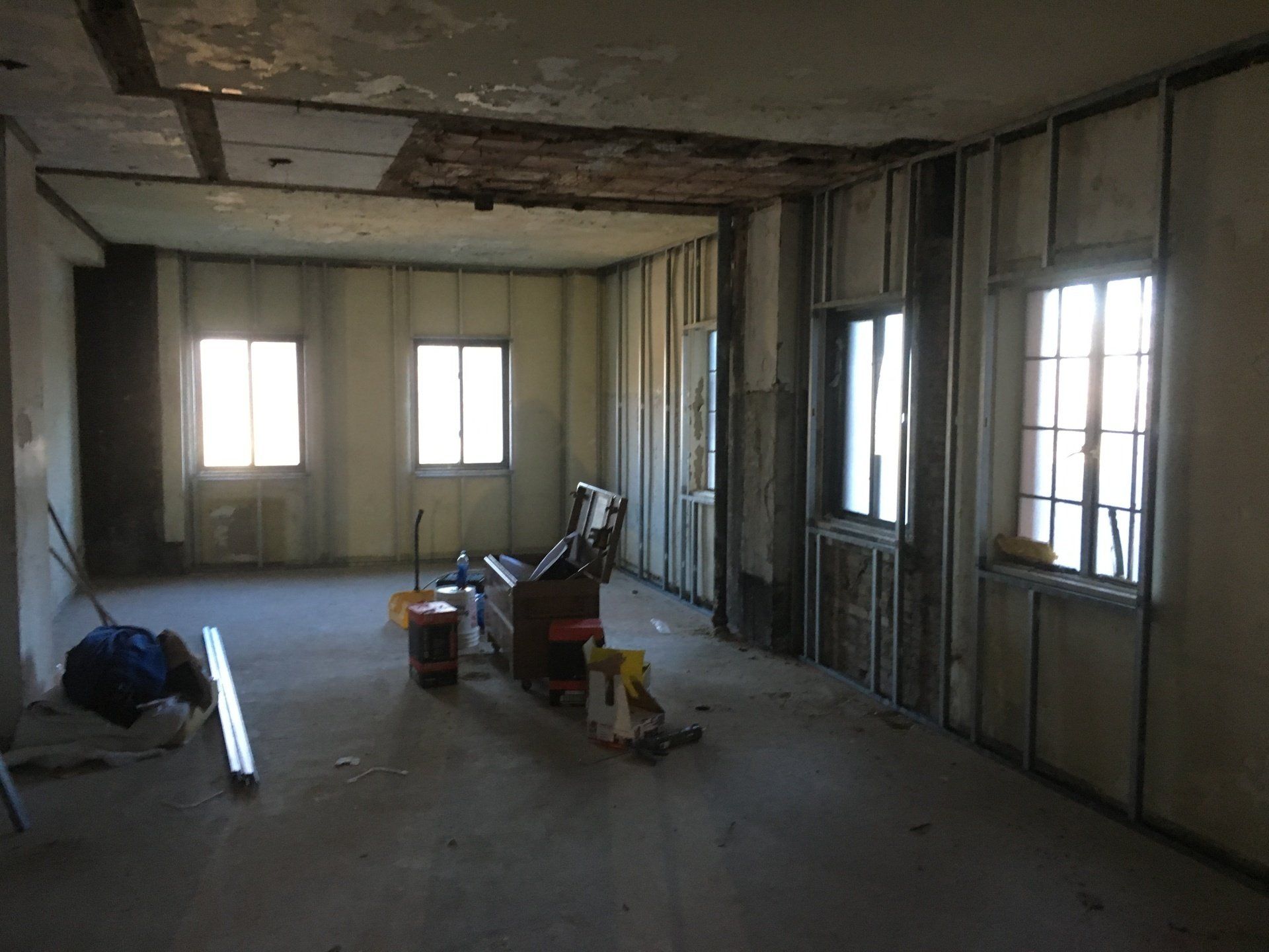 Interior of a room under construction; walls are framed with exposed windows, concrete floor, tools visible.