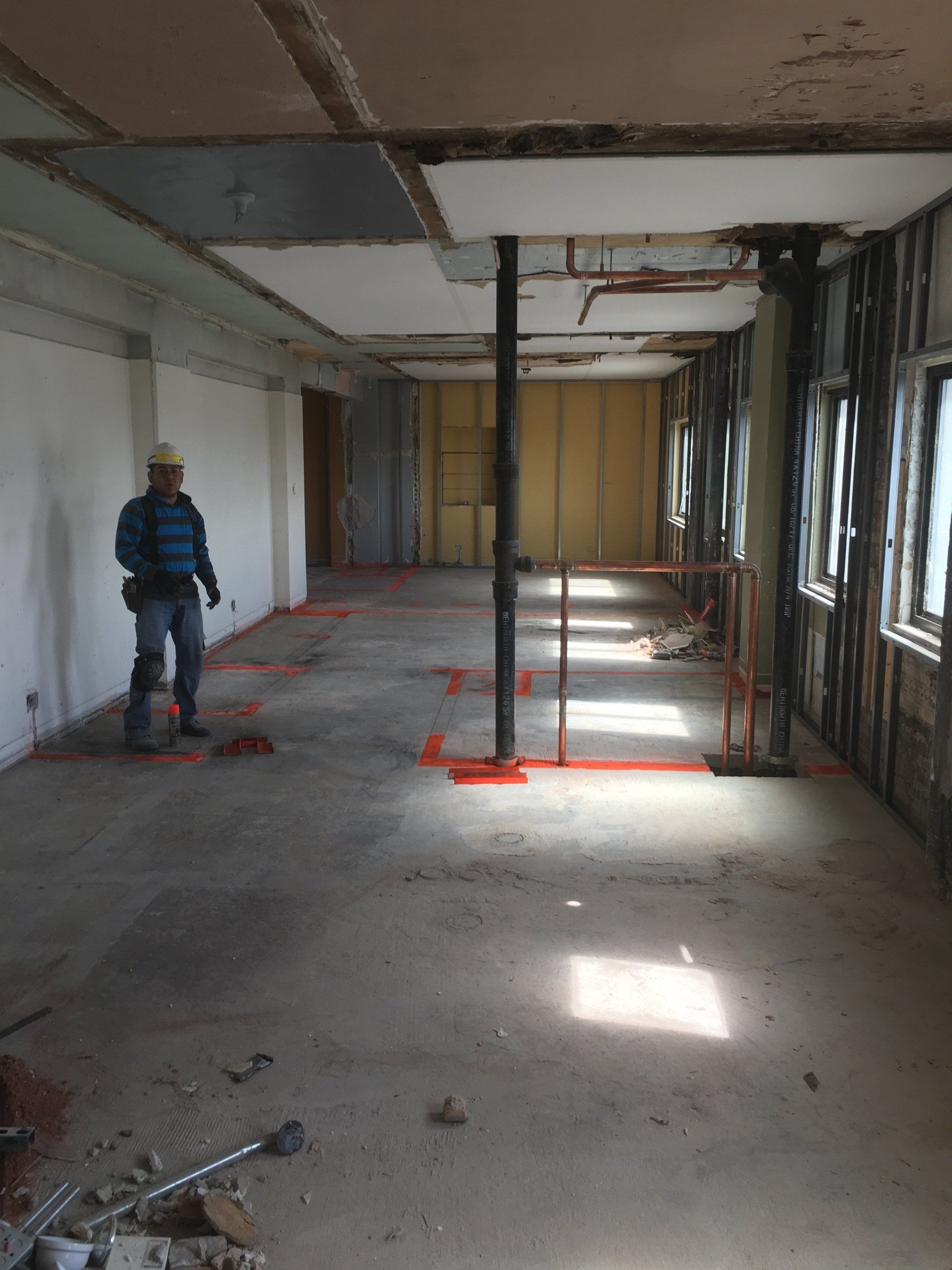 Construction worker in a gutted office space, looking towards the camera. Exposed walls, ceiling. Interior.