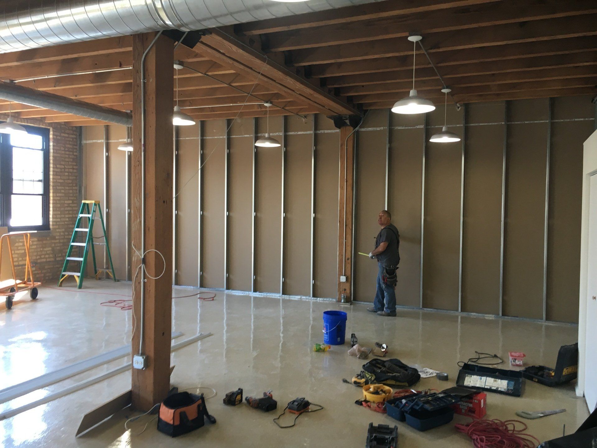Interior construction: man working on wall, tools scattered, unfinished building, exposed beams.