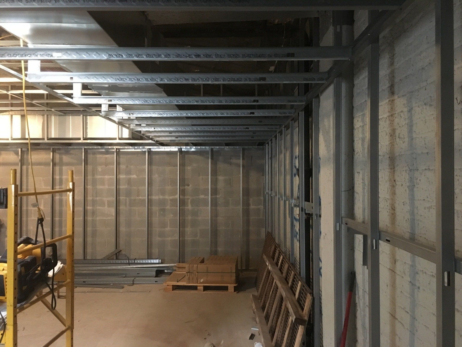 Metal framing for a wall and ceiling in an unfinished room. Construction materials and scaffolding present.