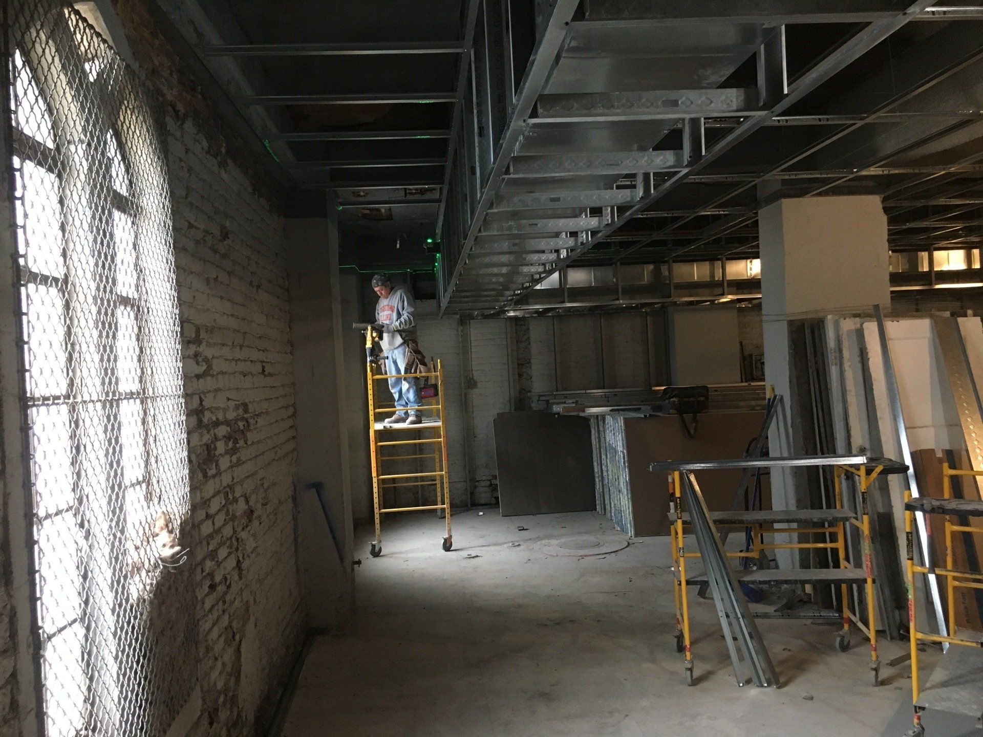 Construction site with person on ladder. Exposed ceiling beams, brick wall with arched window.