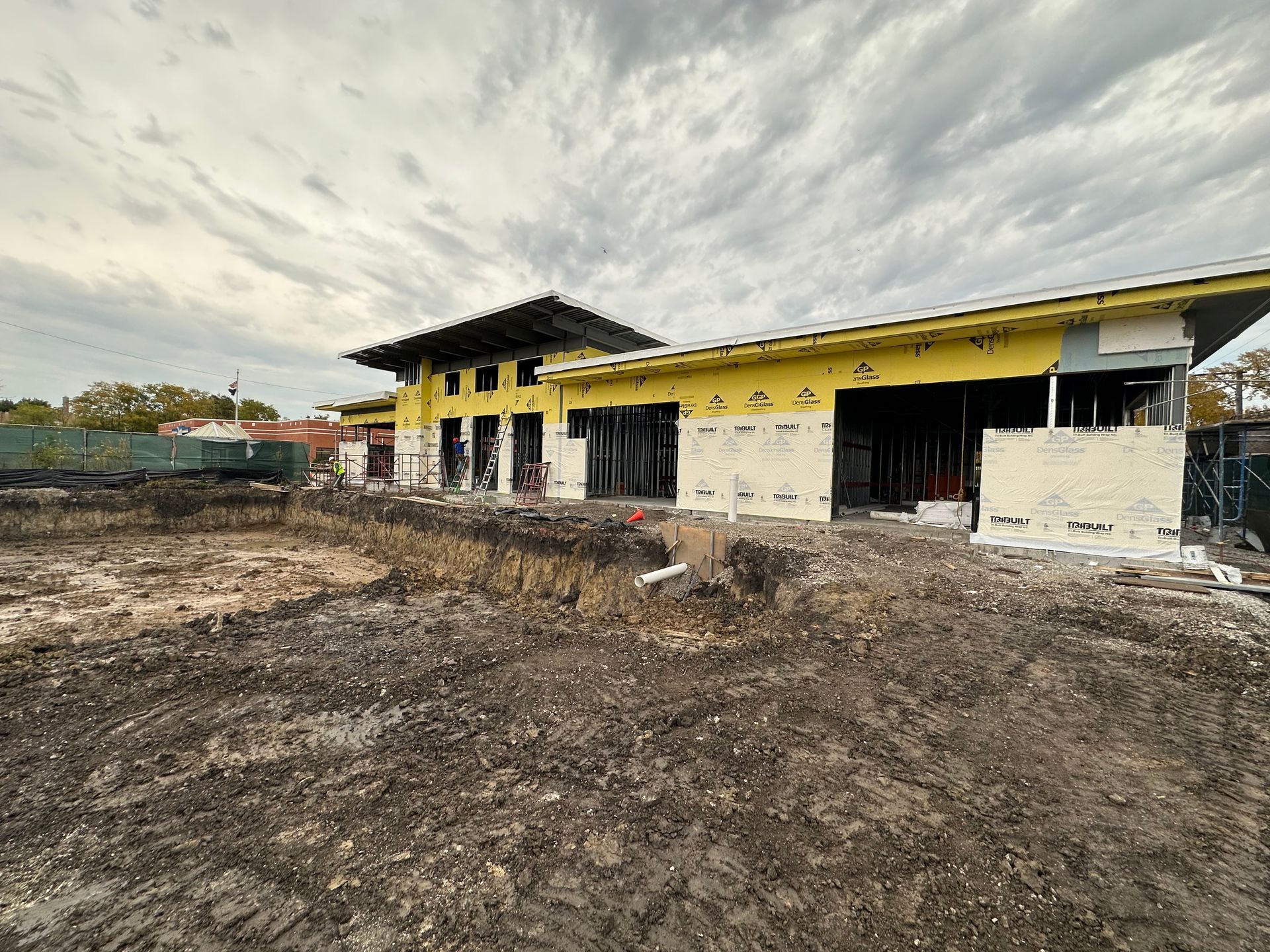 Construction site of a building with exposed framing and insulation, cloudy sky overhead.