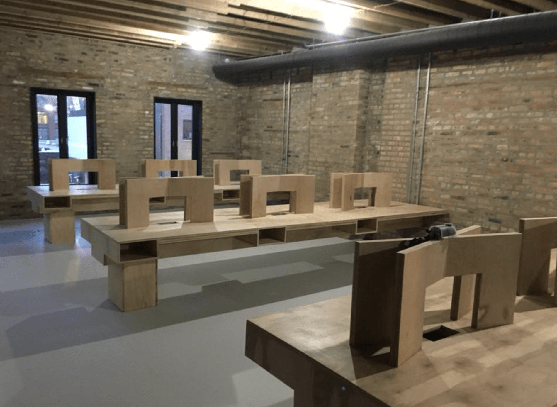 Large room with light brown tables, brick walls, and windows.