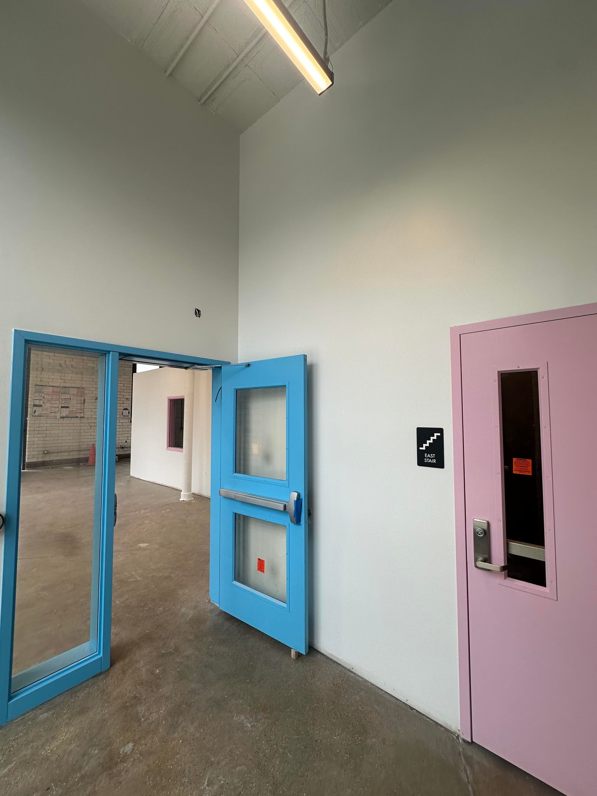 Hallway with open blue doors, pink door on the right, concrete floor, white walls.
