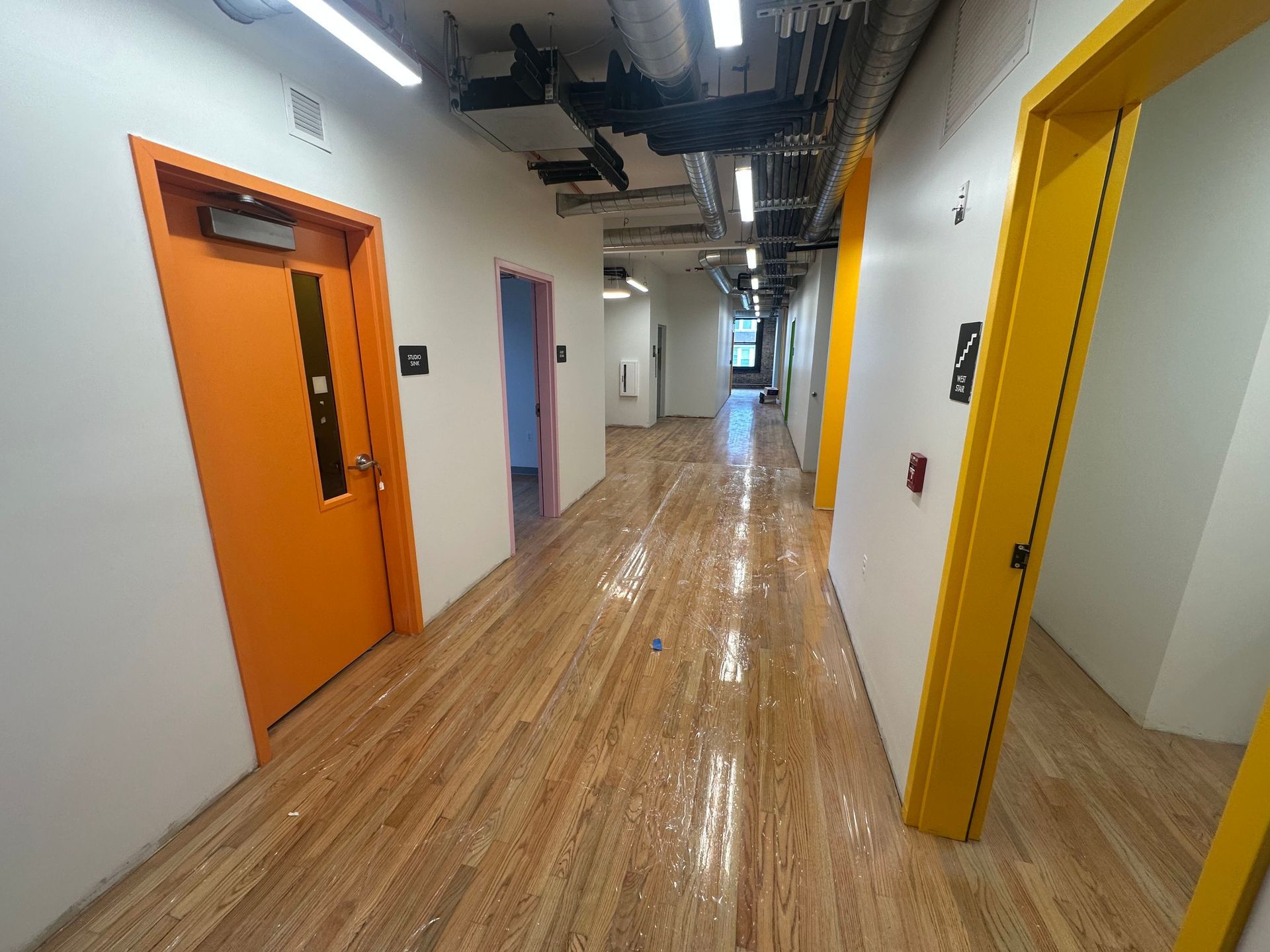 Hallway with orange and yellow doorways, light wood floors, and white walls.