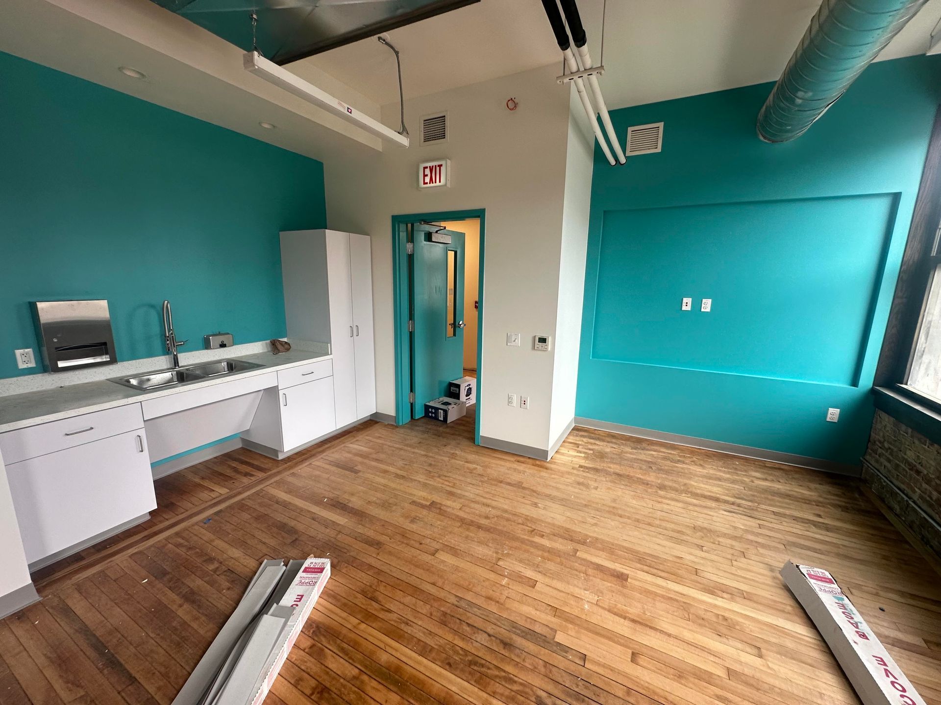 Empty room with teal walls, white cabinets, and wood flooring; door open to another room.